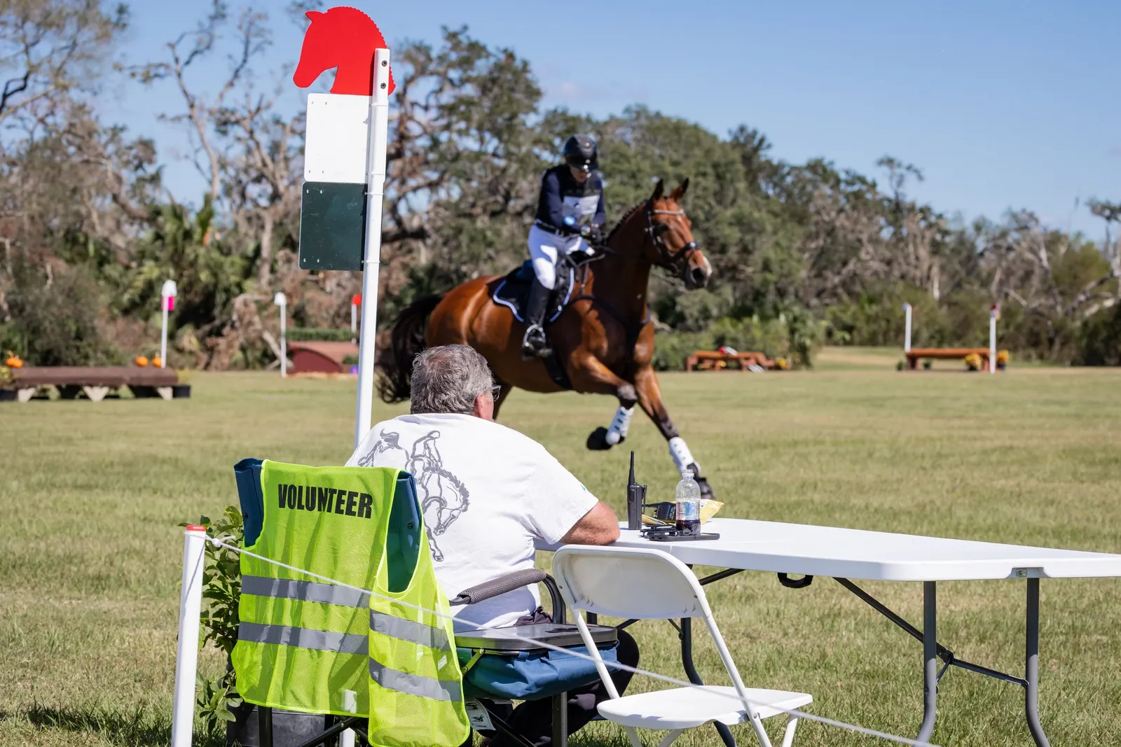 A volunteer in a safety vest watching a horse and rider gallop past on the cross-country course at The Event at TerraNova. Photo by EQ Media.