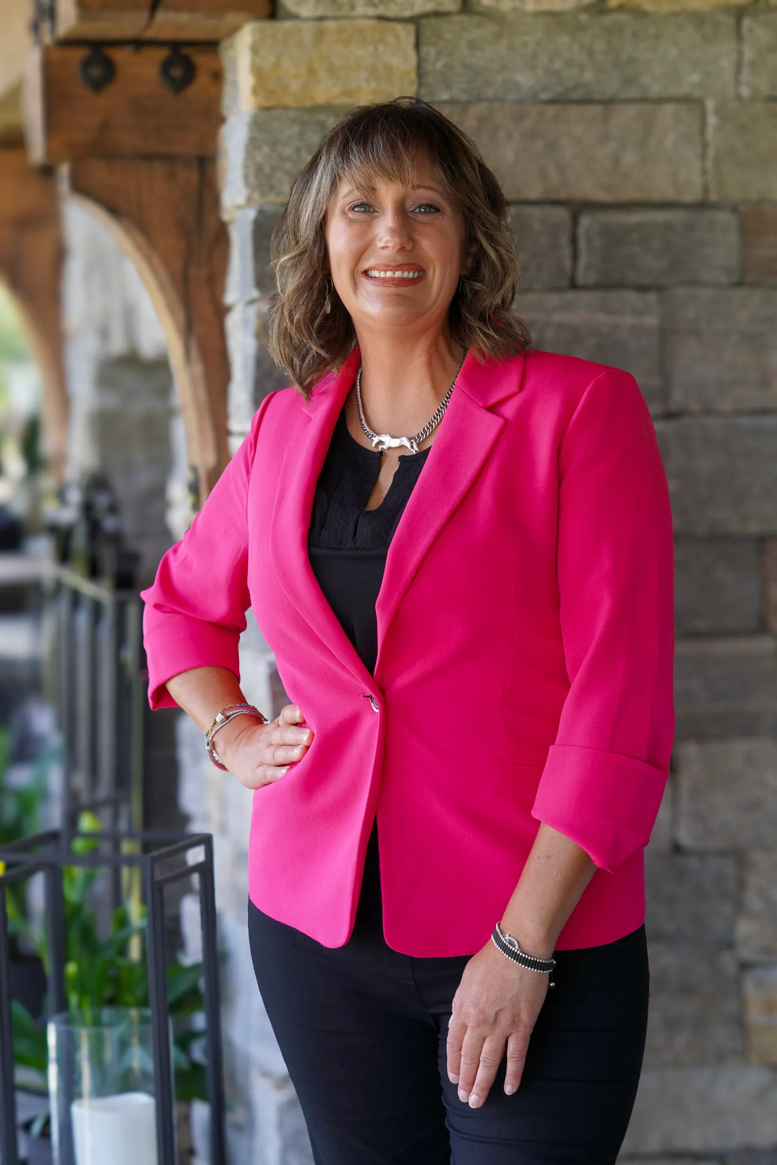 Molly Oakman smiling in a bright pink blazer beneath a stone archway at TerraNova Equestrian Center