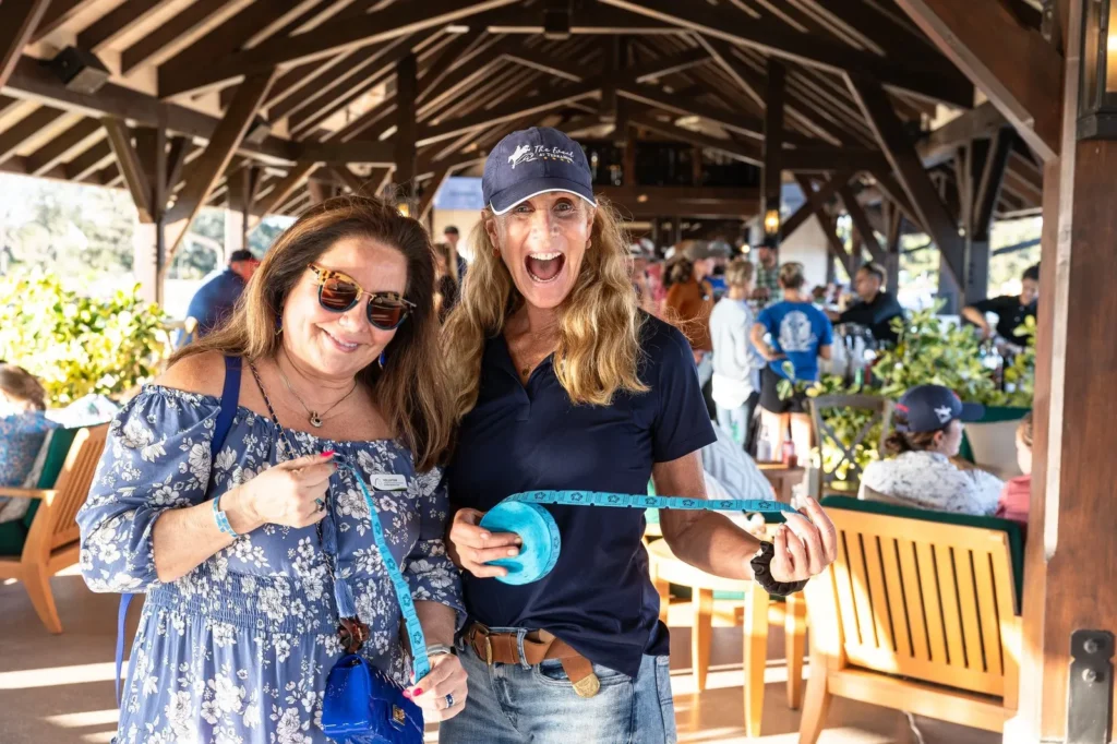 Two smiling TerraNova volunteers holding a blue measuring tape in the hospitality pavilion at TerraNova Equestrian Center